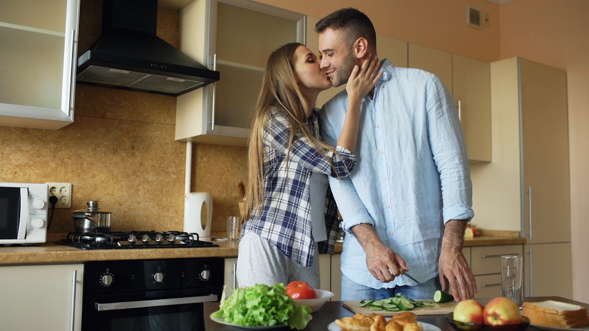 Happy young couple embracing and talking in the kitchen while cooking breakfast at home in the morning