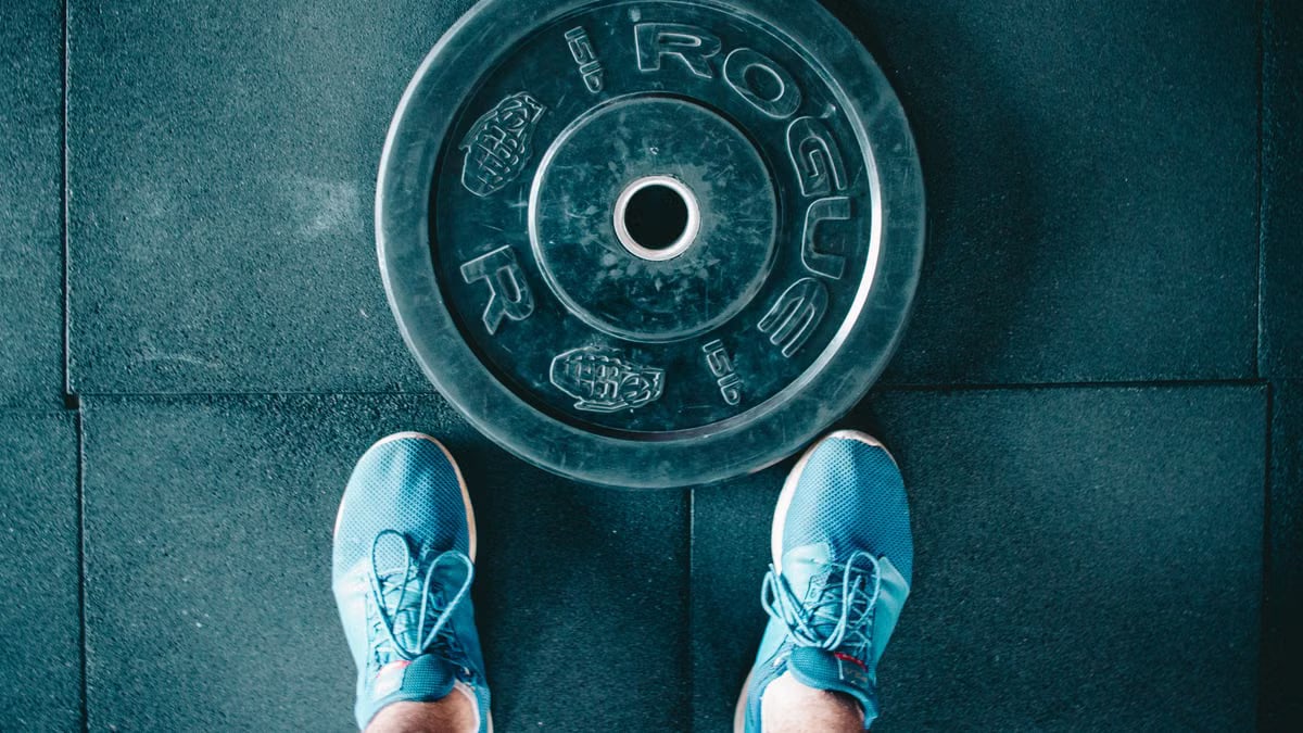 Blue sneakers next to a weight plate on a gym floor, top view.